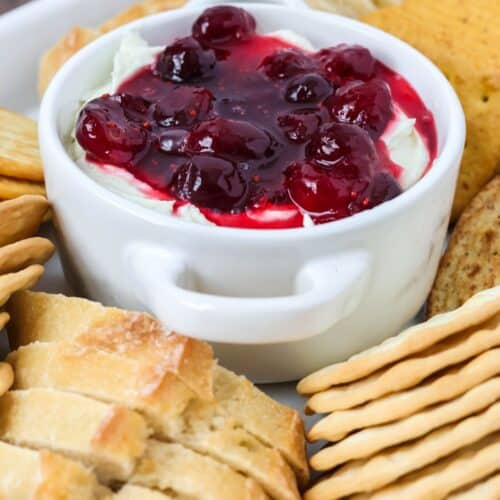 Cranberry Boursin dip served in a small dish, surrounded by crackers and sliced baguette pieces.