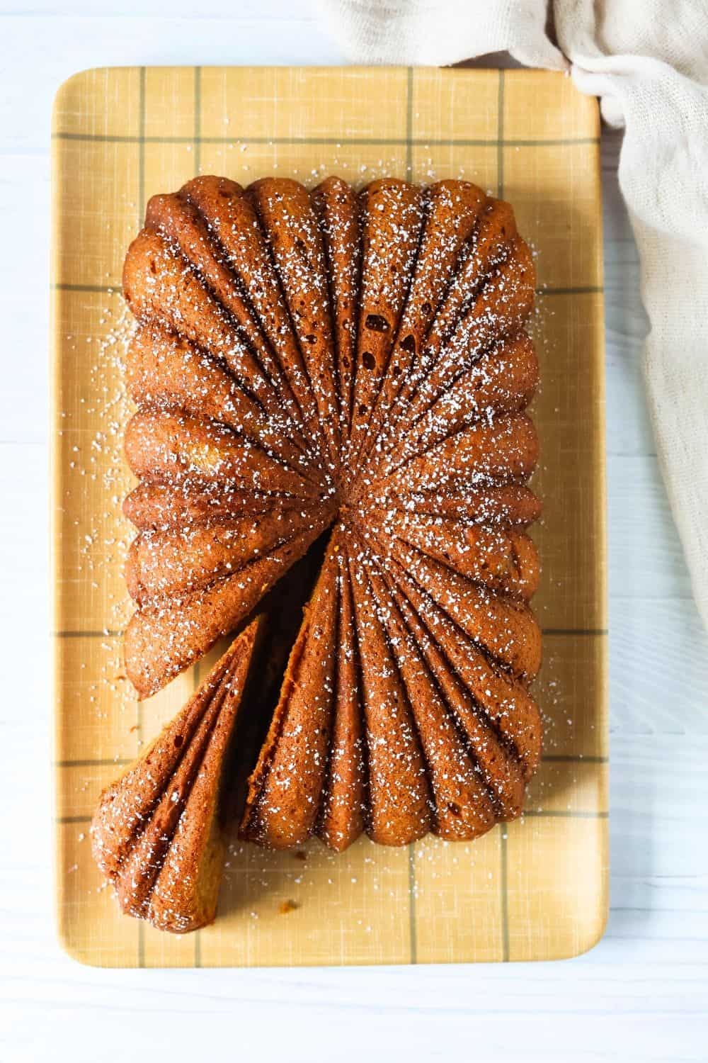 overhead view of a loaf of easy pumpkin bread that was baked in a fluted loaf pan. The loaf is dusted with powdered sugar, and a small wedge has been cut out of the decorative loaf.