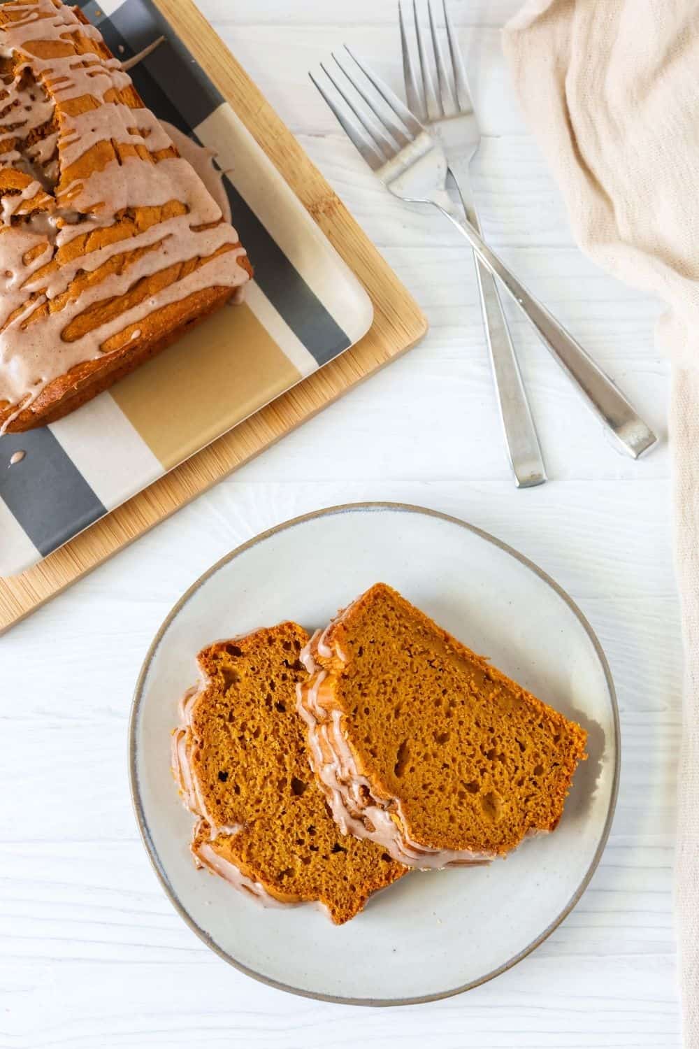 overhead view of an ivory-colored plate with two slices of easy pumpkin quickbread on it, with the remainder of the glazed loaf in the background.