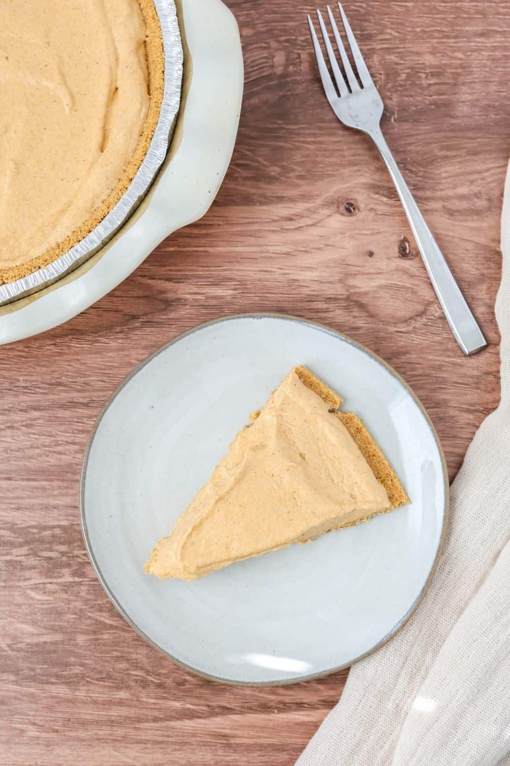 overhead view of a slice of egg-free, no-bake pumpkin pie on a plate, with the remainder of the pie and a fork in the background.