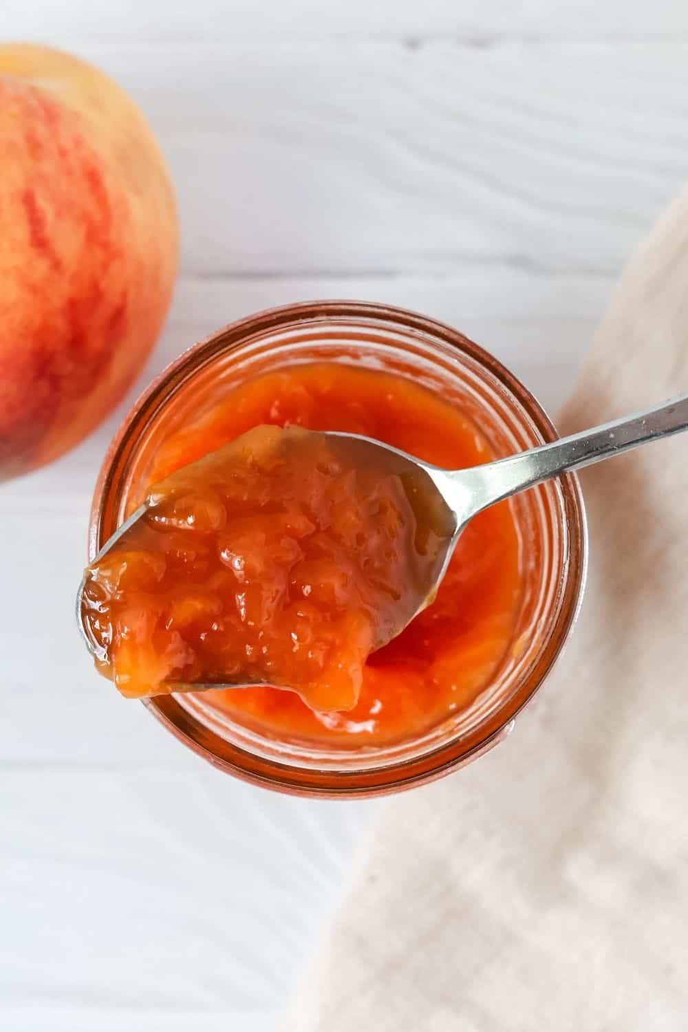 overhead view of a spoon scooping out peach jam from a jar.