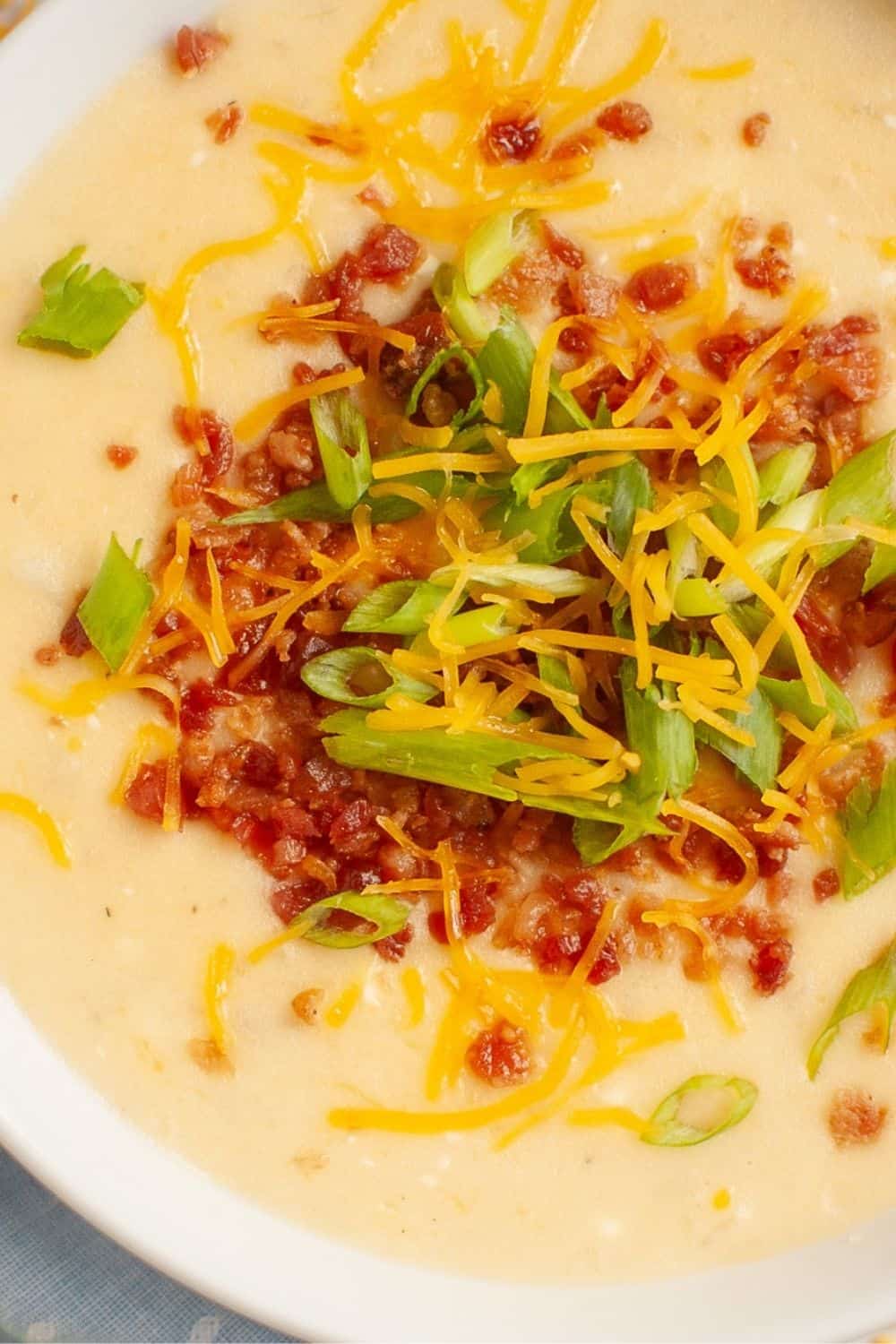 close-up view of a bowl of Instant Pot potato soup with frozen potatoes. It's topped with shredded cheese, bacon crumbles, and sliced green onions.