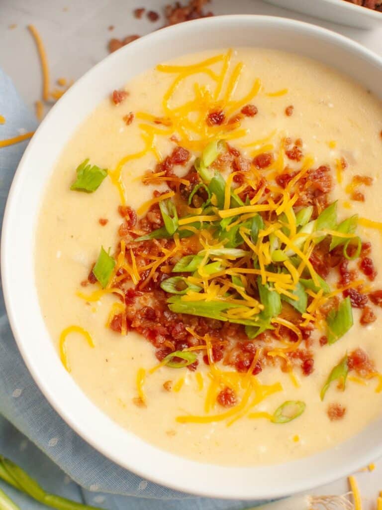 overhead view of a white bowl of Instant Pot potato soup made with frozen hash brown potatoes, garnished with bacon, chese, and green onions.