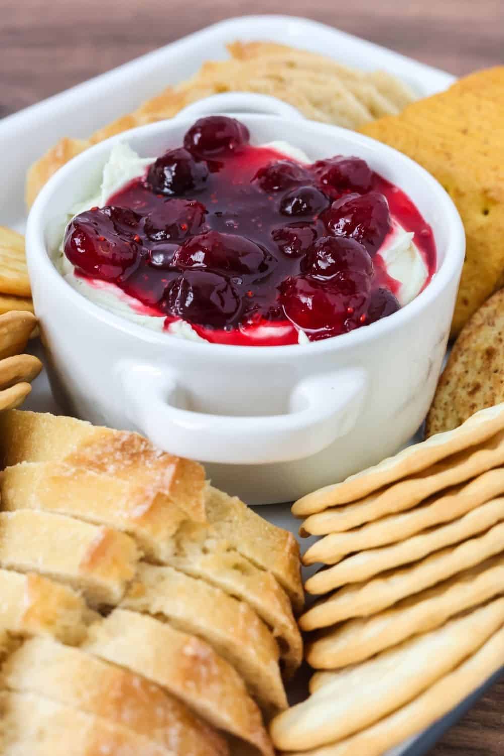 Make ahead cranberry Boursin dip served in a small stoneware dish, surrounded by crackers and bread.