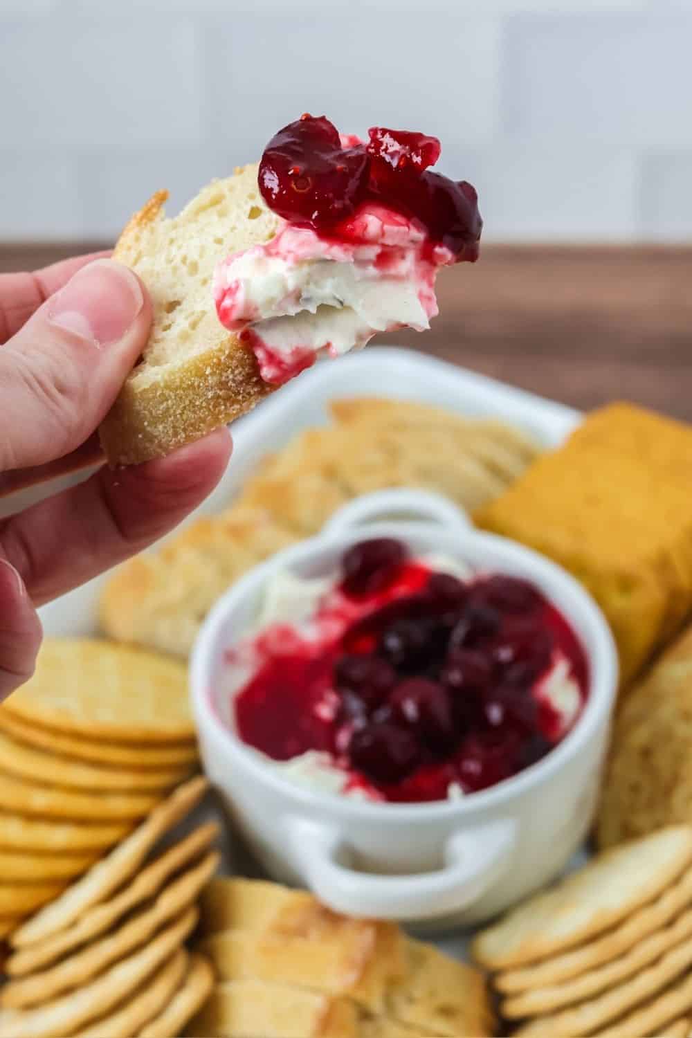 a hand holds a piece of baguette with Boursin cranberry dip spread on it.