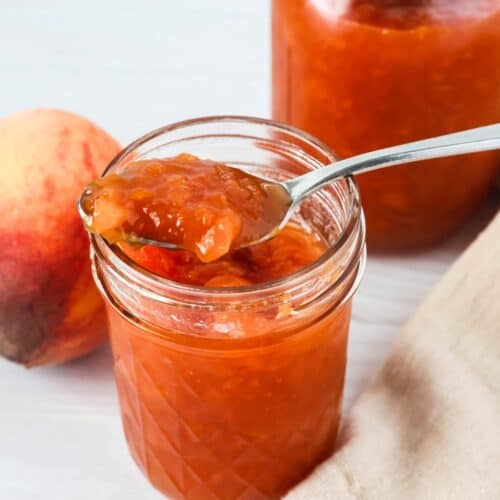 two jars of peach jam, with a spoon in one of the jars.