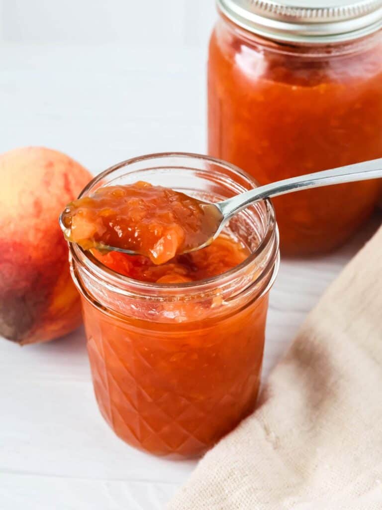 two jars of peach jam, with a spoon in one of the jars.