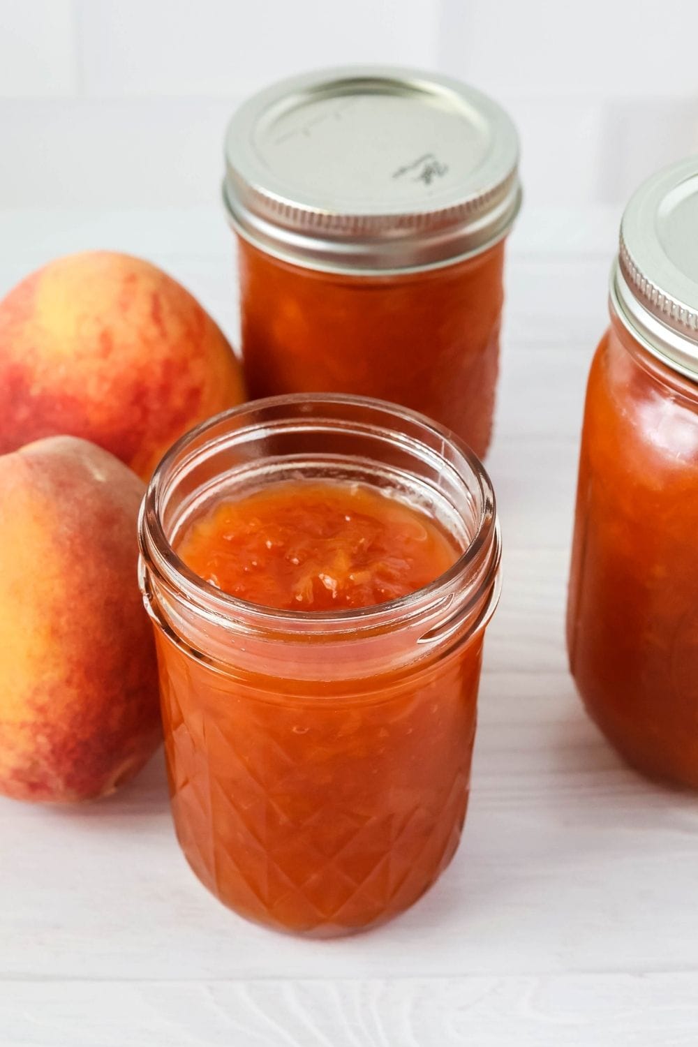 three jars of peach jam made with unpeeled peaches. One of the jars is open.
