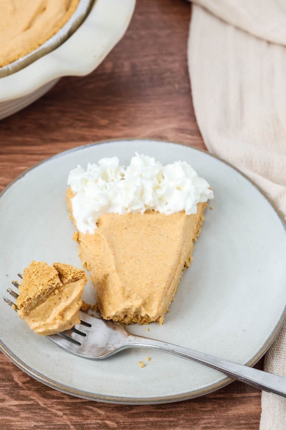 a slice of no bake pumpkin cream pie on a plate, alongside a fork that has removed a bite from the slice.