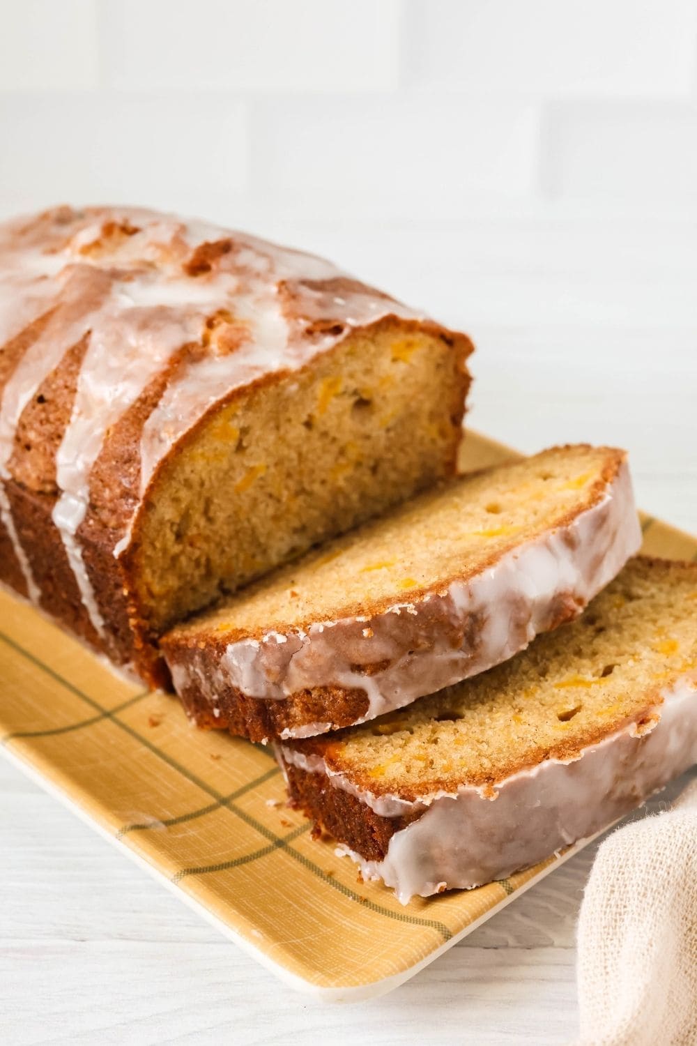 side view of a sliced loaf of peach quickbread made with canned peaches, topped with powdered sugar glaze.
