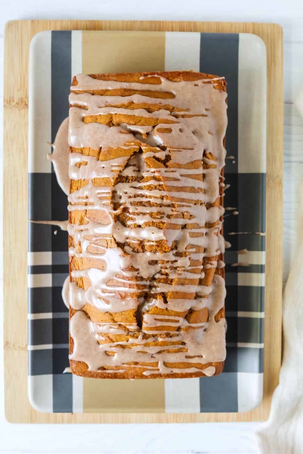 overhead view of a loaf of cake mix pumpkin bread on a plaid-patterned plate. The bread is topped with a cinnamon icing glaze.