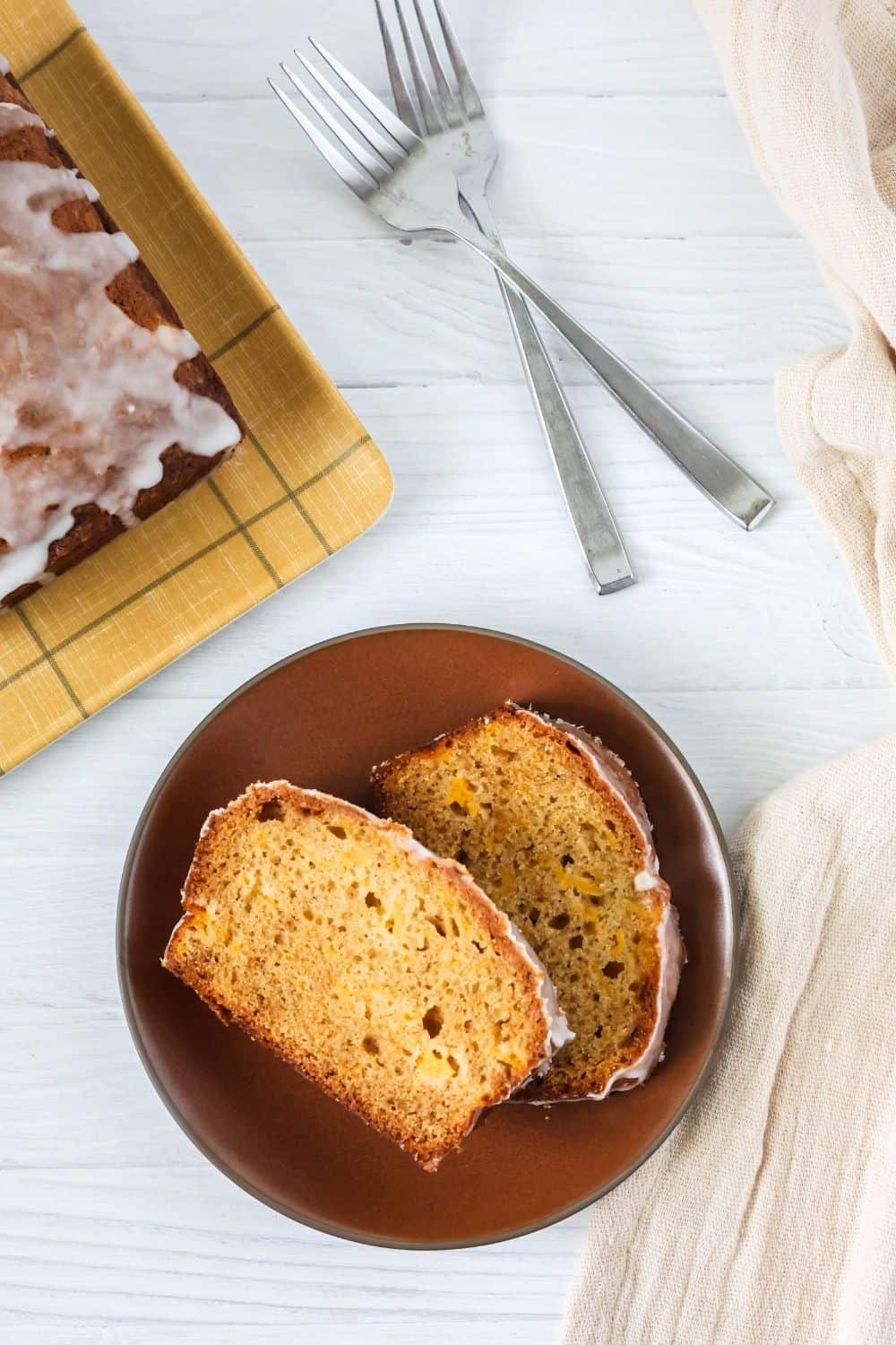 two slices of southern peach bread on a brown plate, with forks and the remaining loaf of bread in the background.