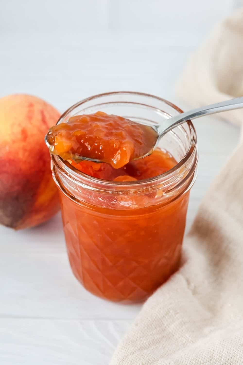 a spoon scoops some peach jam made without pectin from a jar.