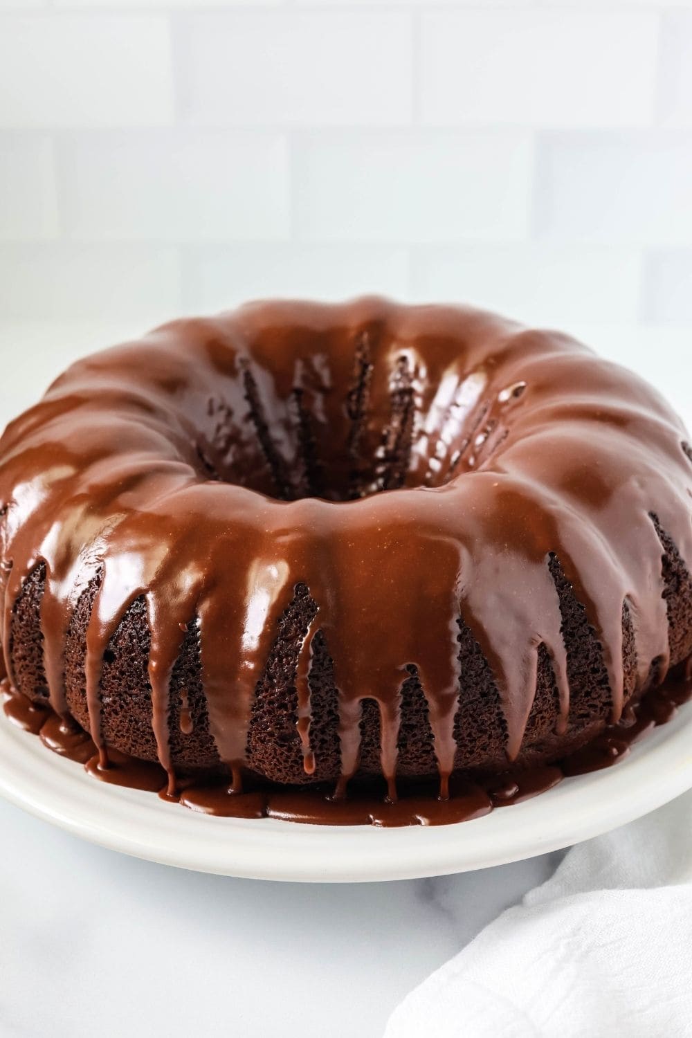 southern chocolate mayonnaise bundt cake, made from a cake mix, served on a white plate and topped with chocolate glaze.
