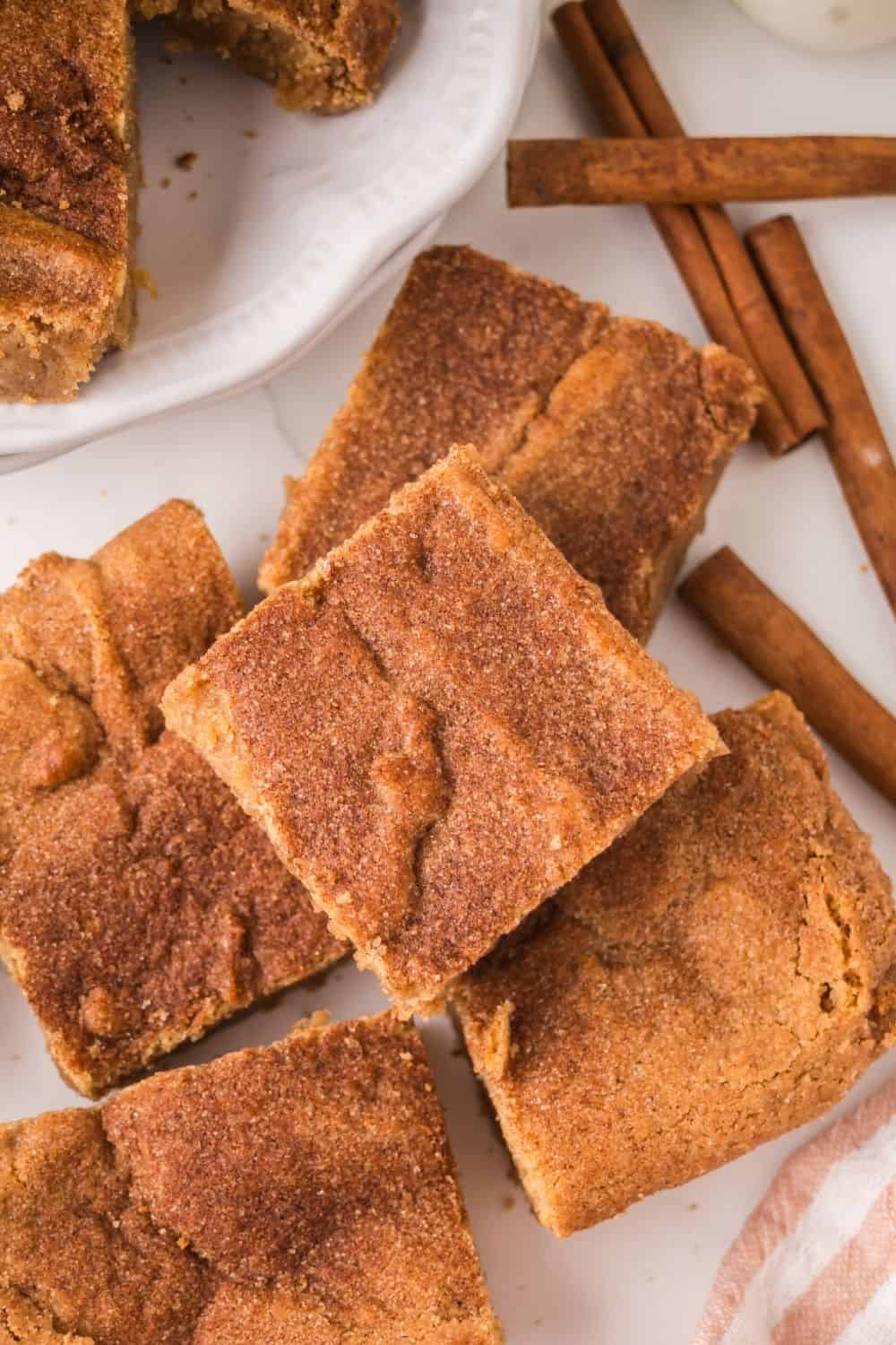overhead view of a few squares of churro dessert bars, with cinnamon sticks nearby.