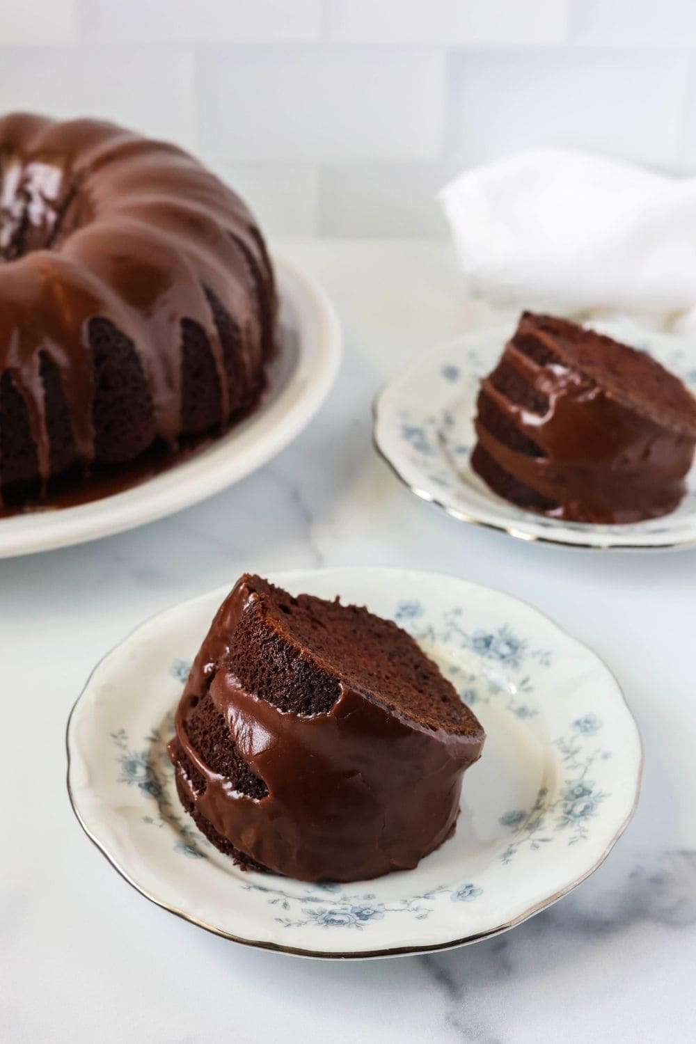 two slices of chocolate mayonnaise cake, made from cake mix, served on plates, with the remaining whole bundt cake in the background.