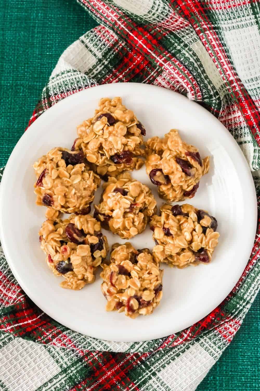 overhead view of several oatmeal cranberry no-bake cookies served on a white plate atop a plaid kitchen hand towel.