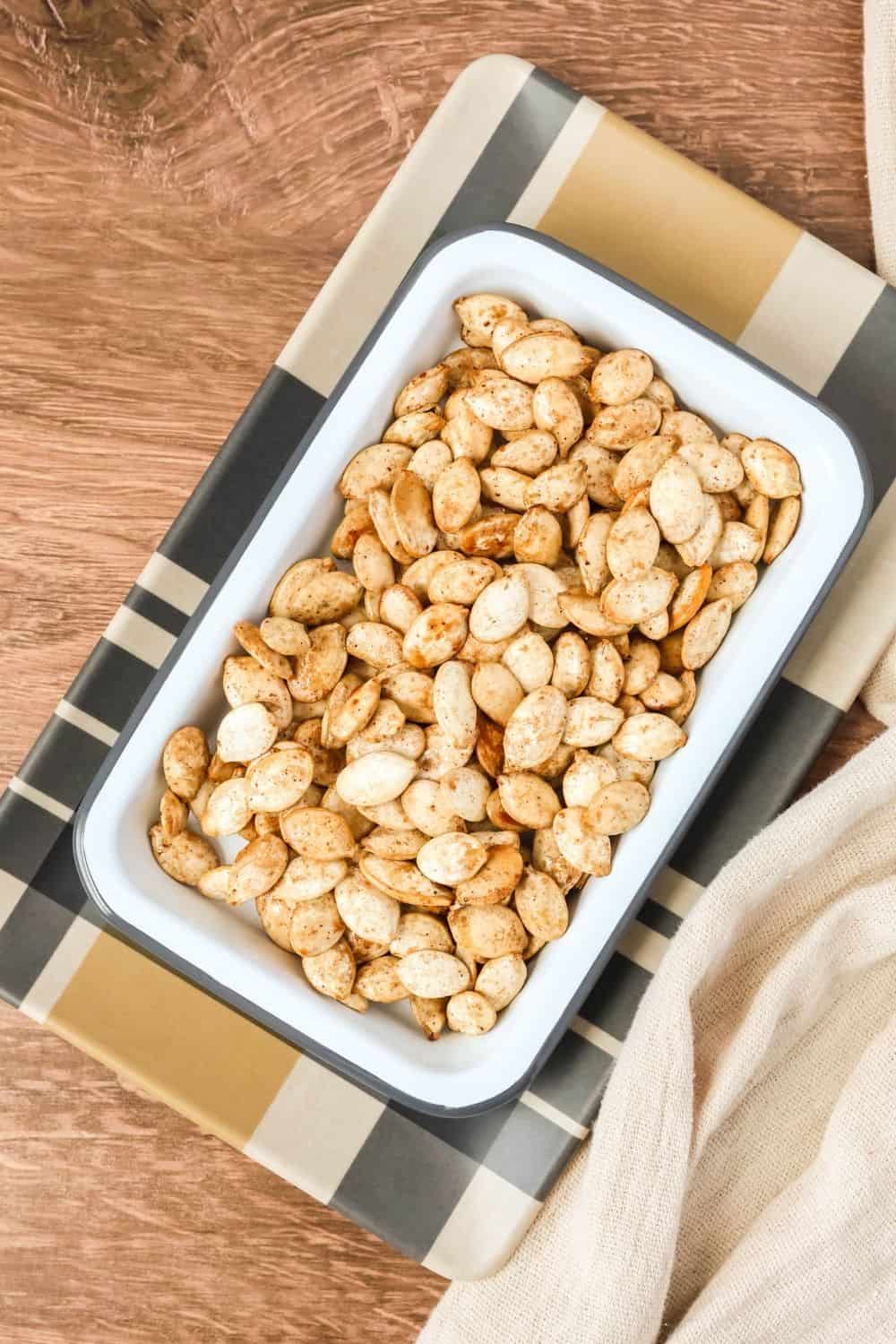 overhead view of a small rectangular dish containing pumpkin seeds roasted in maple syrup and bourbon.