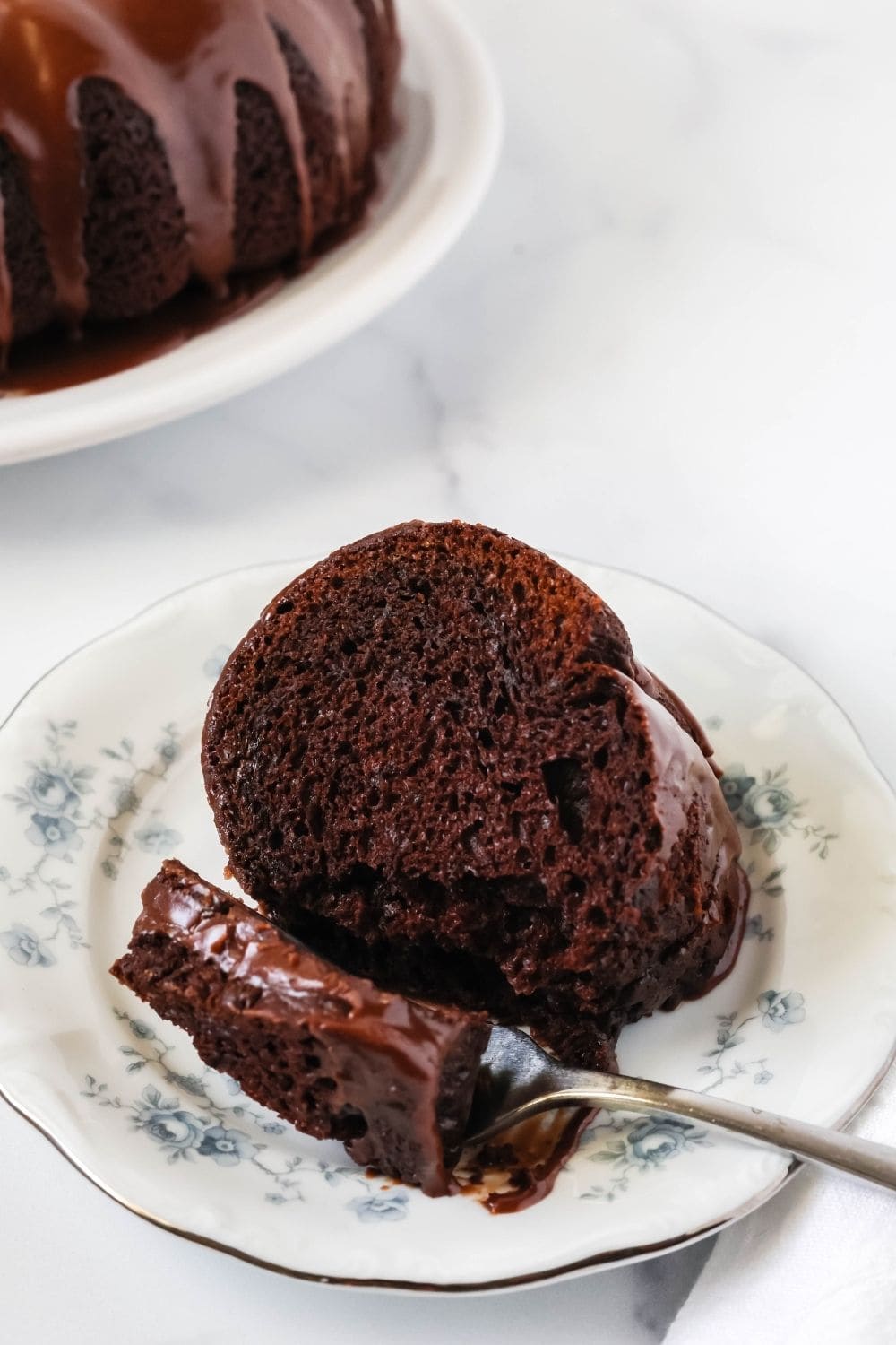 a slice of chocolate mayonnaise cake on a plate. A fork has removed a bite, which is resting next to the slice.