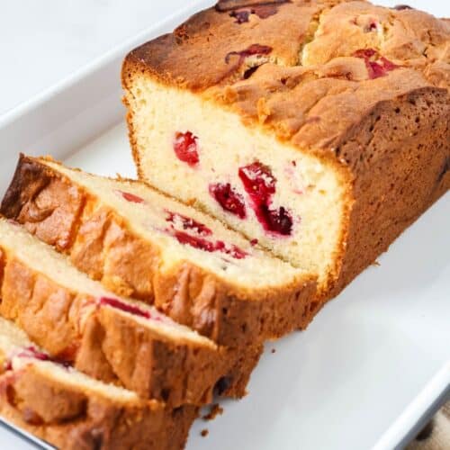 A loaf of cake mix cranberry bread, partially sliced, on a white platter.