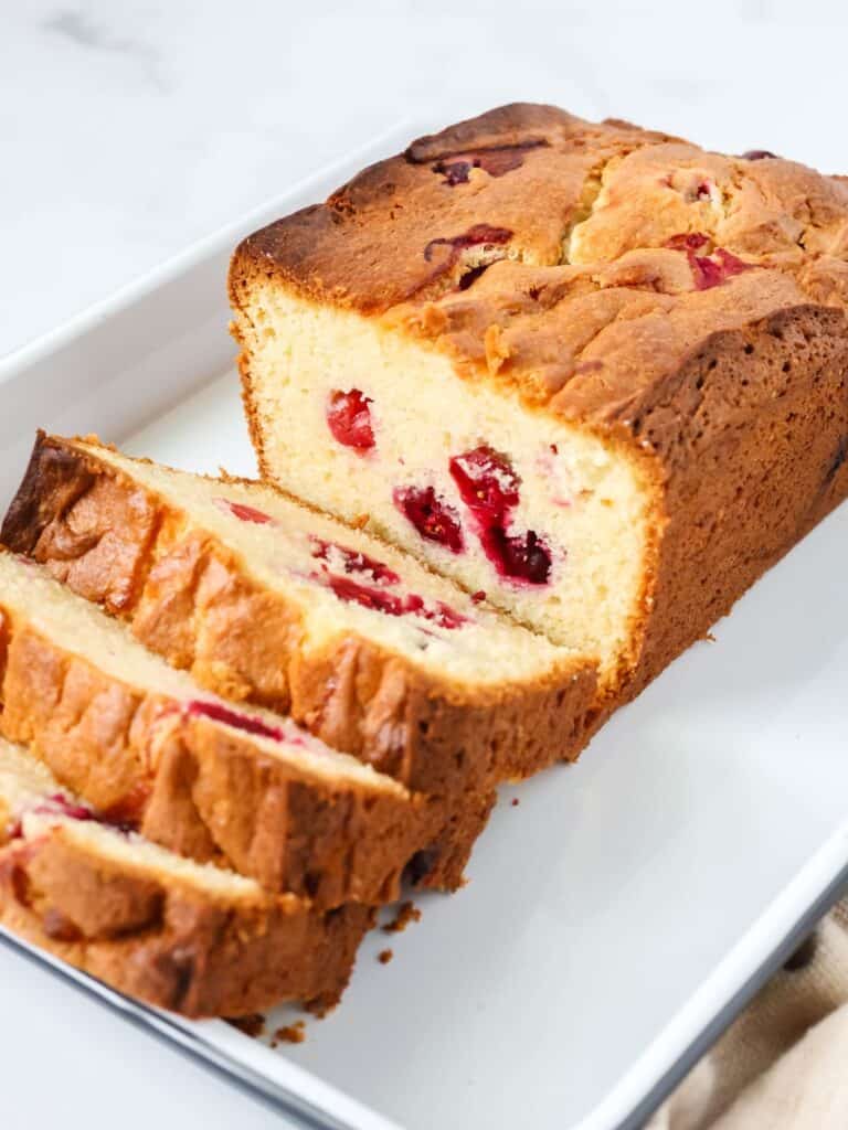 A loaf of cake mix cranberry bread, partially sliced, on a white platter.