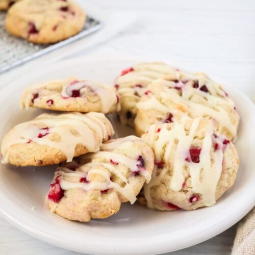 Cake mix cranberry orange cookies served on a white plate. The cookies are topped with a drizzle of icing.
