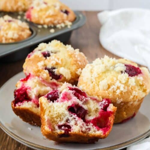 Cake mix cranberry orange muffins served on a plate, with more muffins in the pan in the background. One muffin is torn in half to show the juicy berries inside.