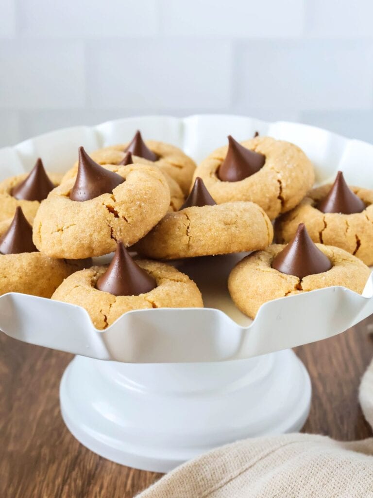 a white dessert stand displays several cake mix peanut butter blossom cookies.