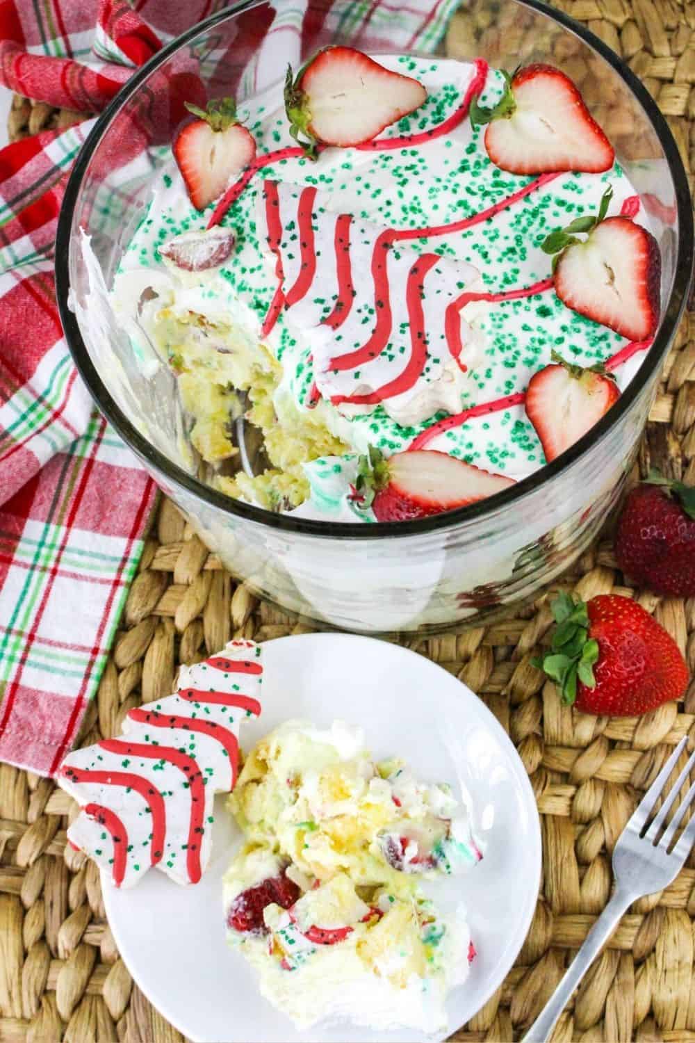 overhead view of a white plate with a serving of Christmas trifle on it, garnished with a Christmas Tree Cake. The glass dish of Christmas no-bake trifle is next to the plate.