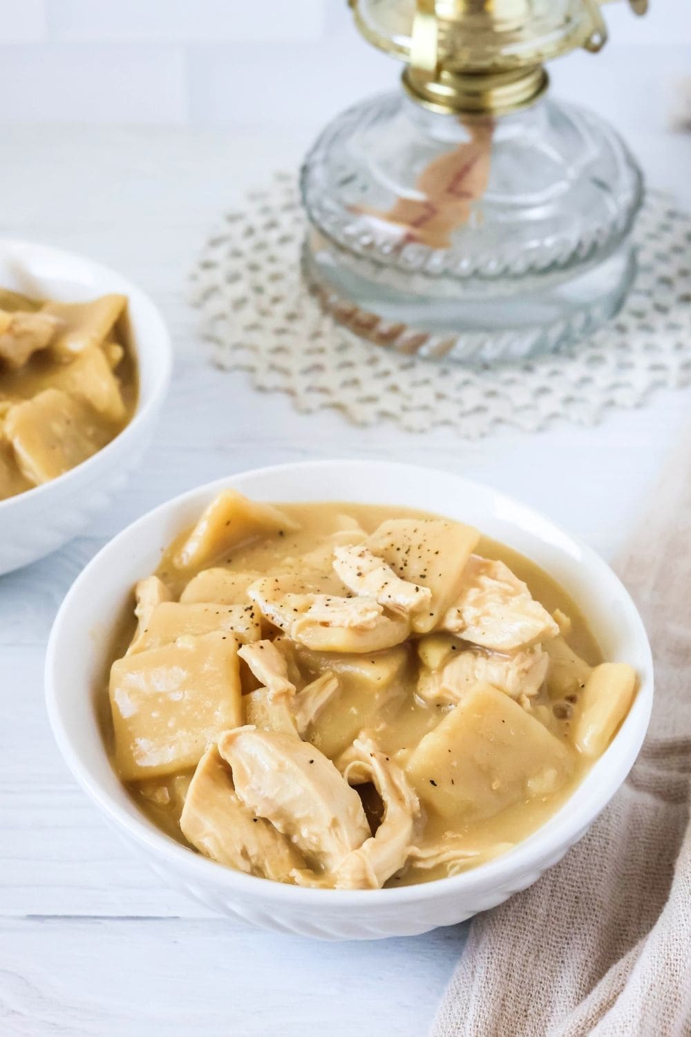 a white bowl of homemade Instant Pot chicken and dumplings like Cracker Barrel's, with another bowl and an oil lamp in the background.