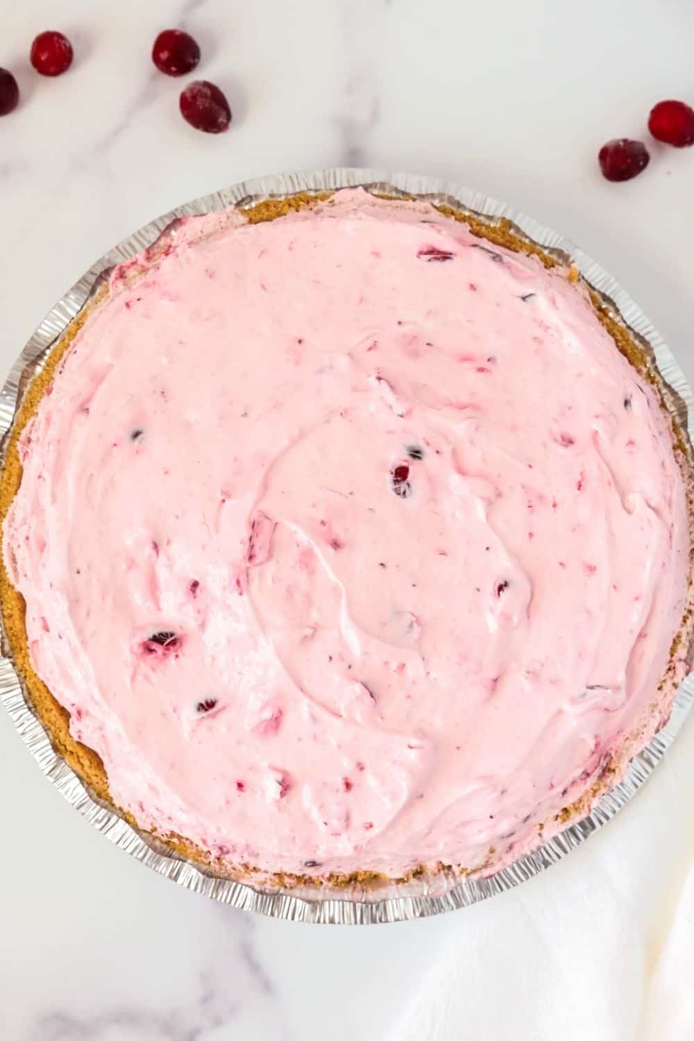 overhead view of a whole cranberry cream pie, with a few fresh cranberries scattered around it.