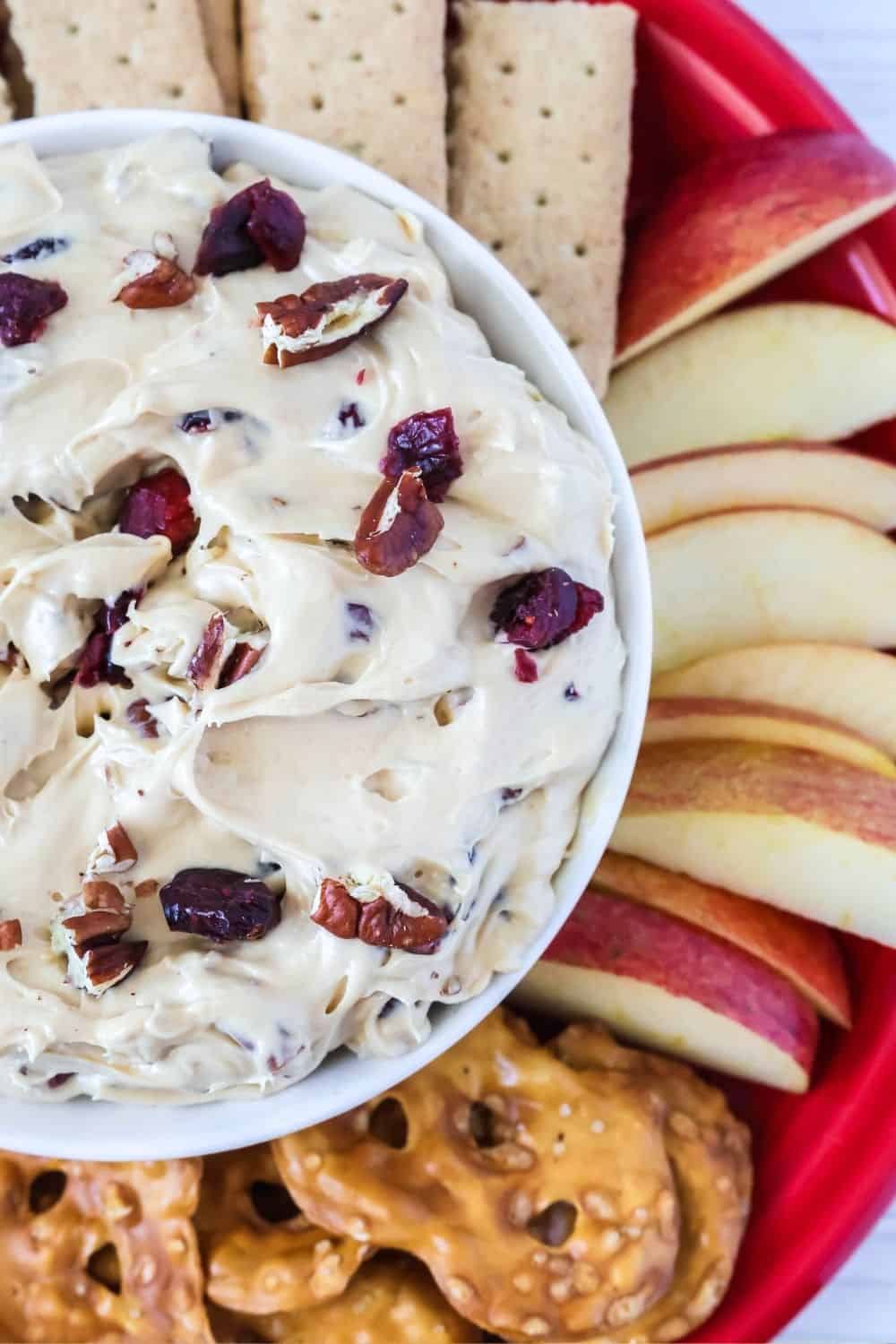 overhead close-up view of a bowl of cranberry pecan cream cheese dip, with pretzels, graham crackers, and apples next to it.