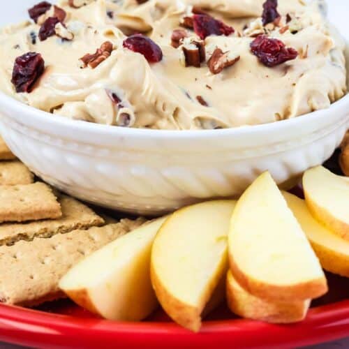 close-up view of cranberry pecan dip in a white bowl, surrounded by graham crackers and apple slices for dipping.