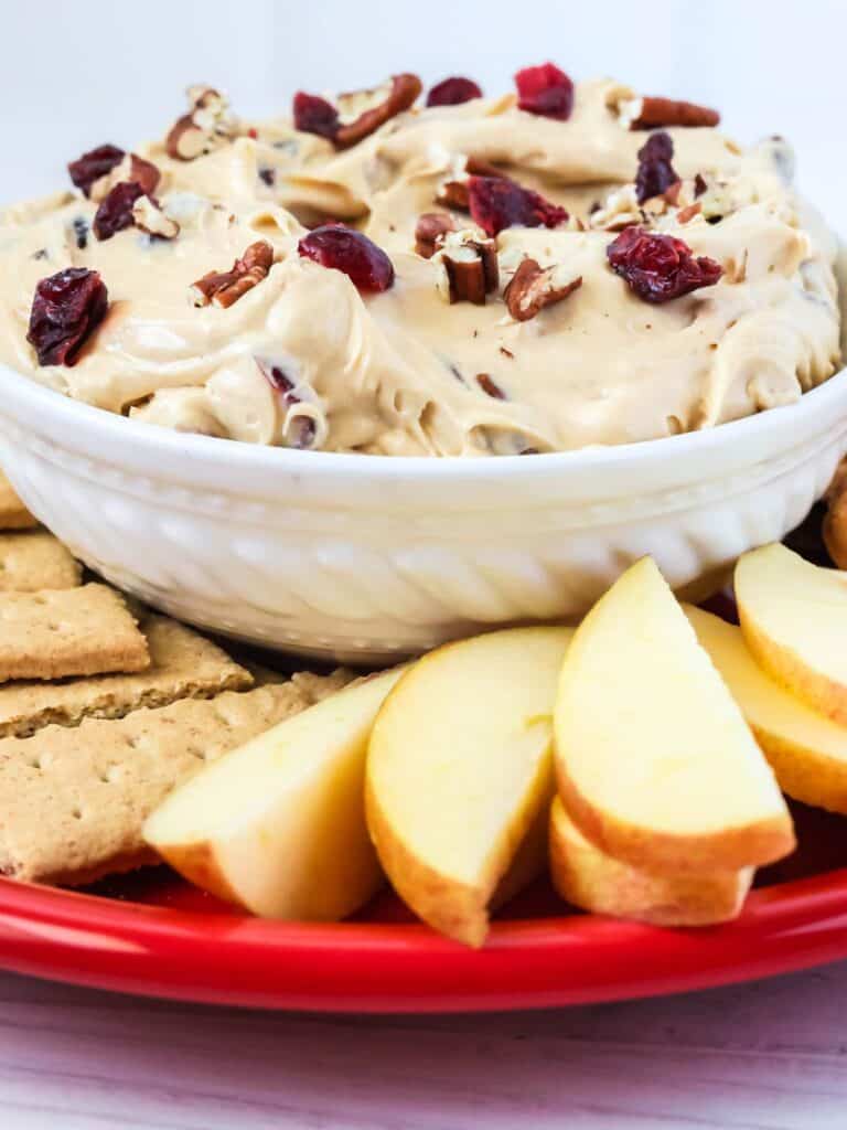 close-up view of cranberry pecan dip in a white bowl, surrounded by graham crackers and apple slices for dipping.