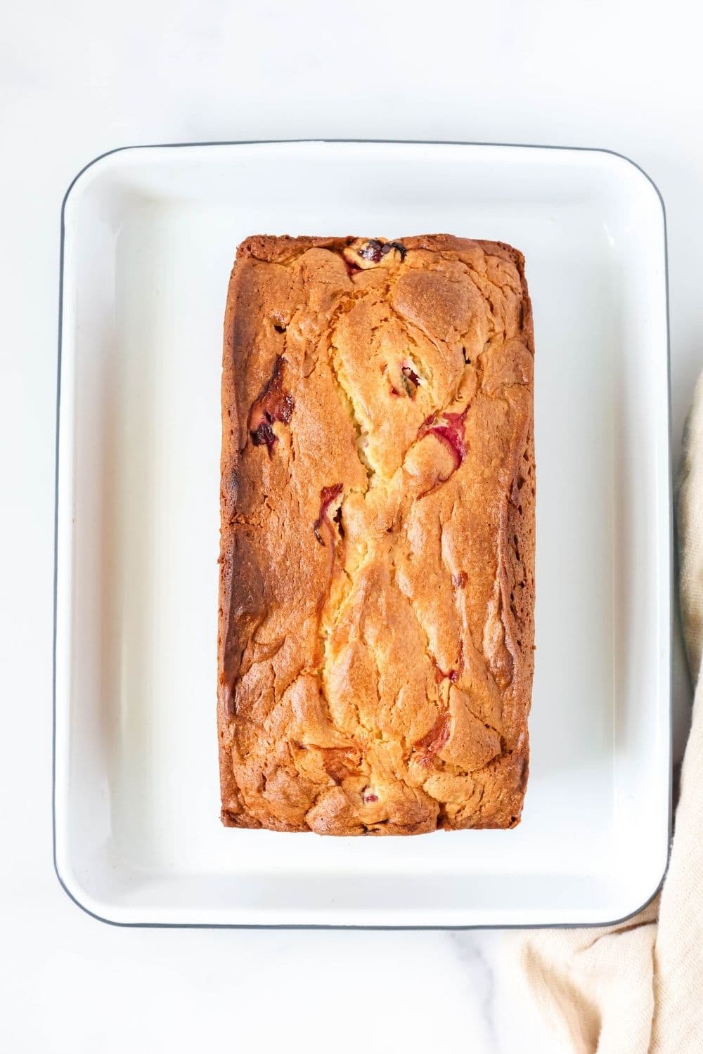 overhead view of a whole loaf of cranberry quickbread made with cake mix, served on a white enamelware platter.