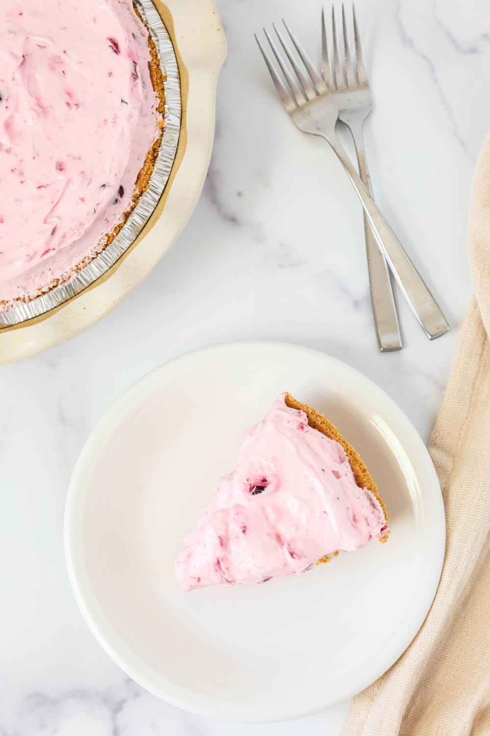 overhead view of a slice of cranberry sauce pie on a white plate, with the remainder of the whole pie in the background, along with two forks.