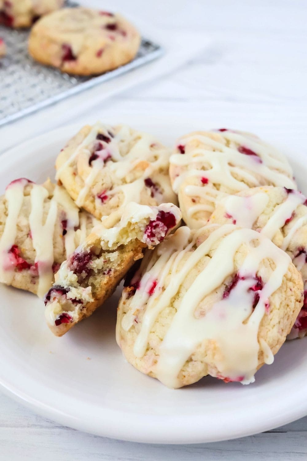 several cranberry orange cookies on a white plate; one cookie has a bite taken out of it, showing its soft and chewy interior.