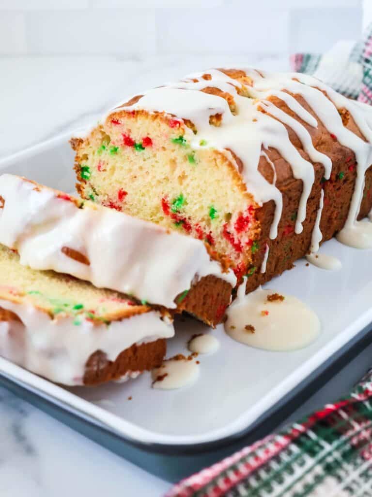 Funfetti Christmas bread loaf topped with icing and sliced, showing the red and green sprinkles in the bread.