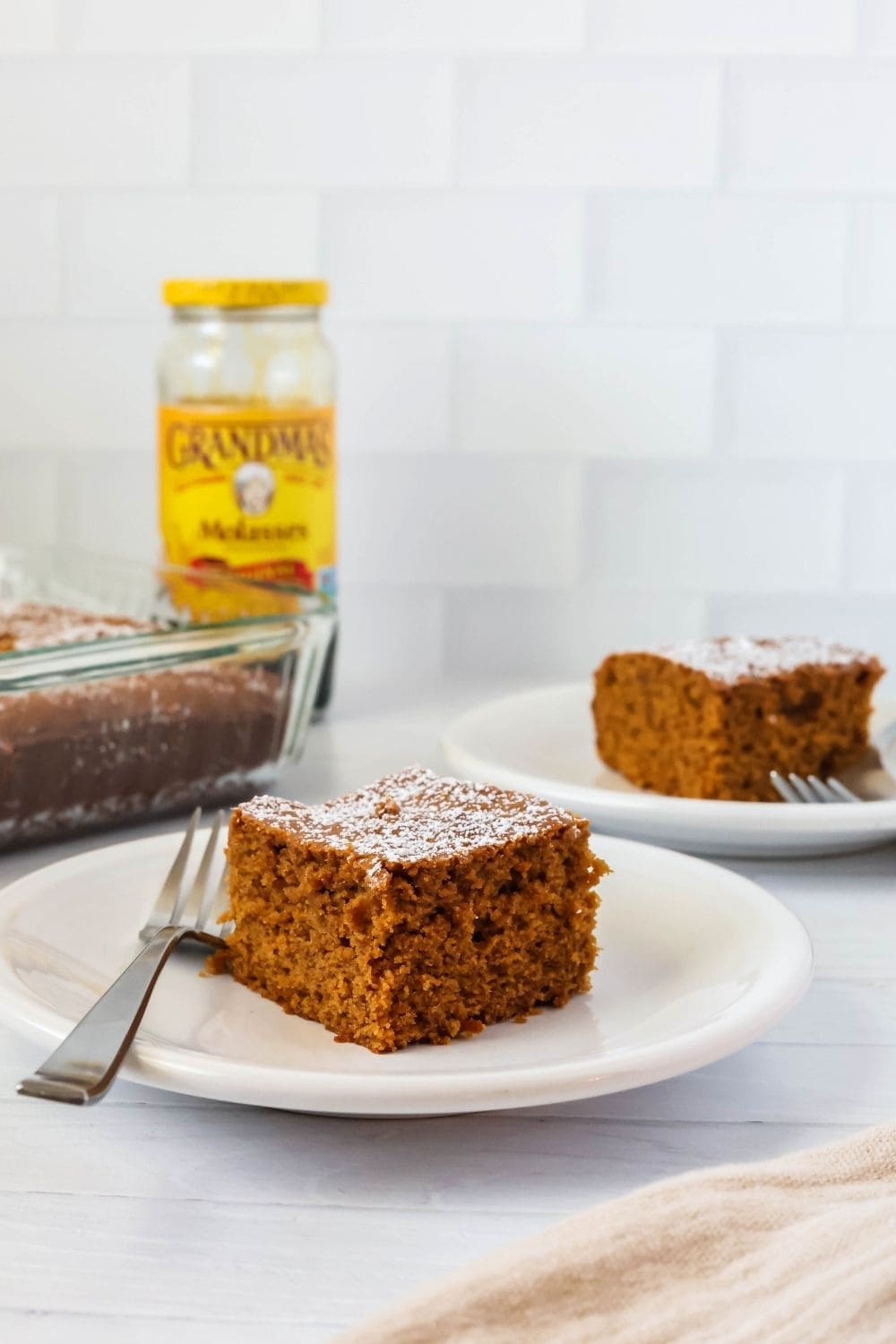 two dessert plates, each with a square of molasses cake on it. A bottle of Grahdma's brand molasses is in the background next to the cake pan.
