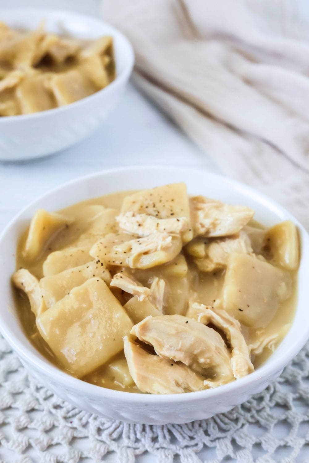 two white bowls of Instant Pot chicken and flat dumplings.