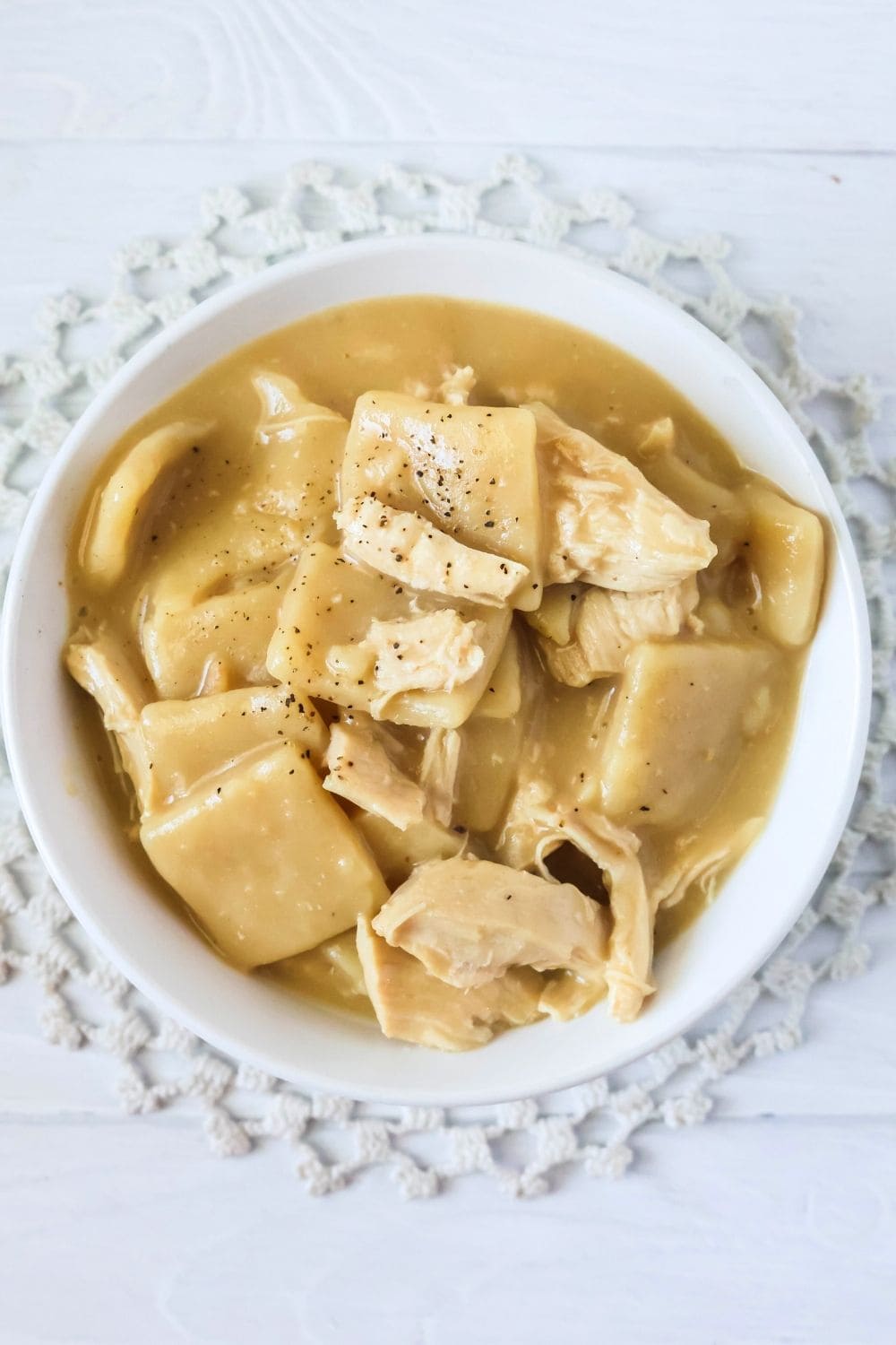 overhead view of a bowl of Instant Pot Cracker Barrel chicken and dumplings set on top of a crocheted doily.