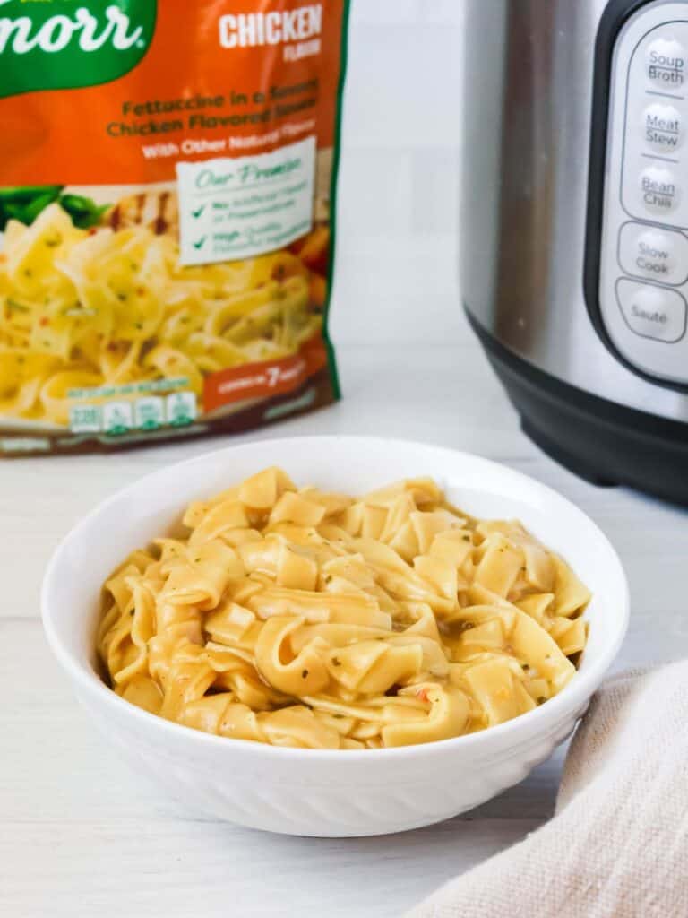 a bowl of Instant Pot Knorr pasta sides, with a package of Knorr sides and a pressure cooker in the background.