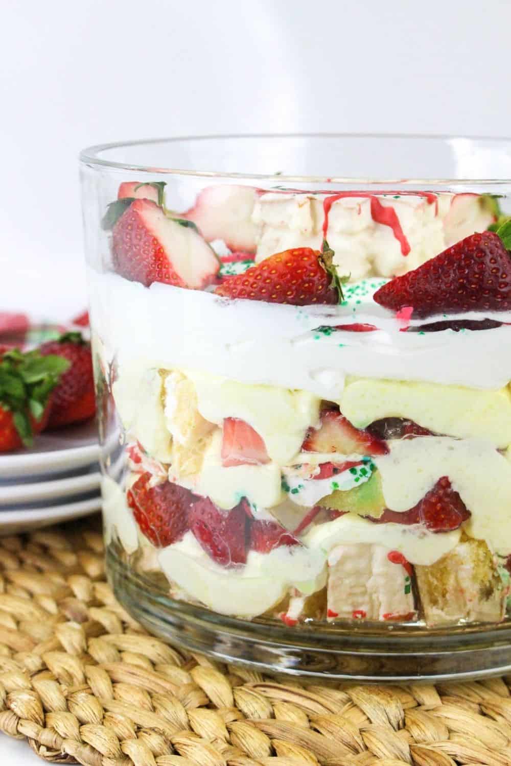 side view of a trifle dish, showing the layers of Christmas Tree cakes, vanilla pudding, whipped cream, and strawberries.