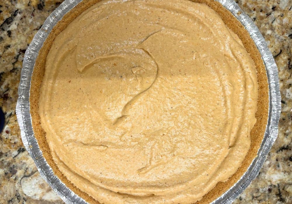 overhead view of a storebought graham cracker crust in a pie tin, filled with no-bake pumpkin pie filling.