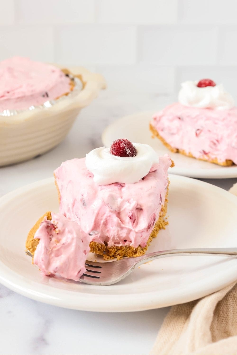 a slice of no-bake cranberry cream pie on a white plate. A fork has cut a bite out of the pie and is resting next to it.