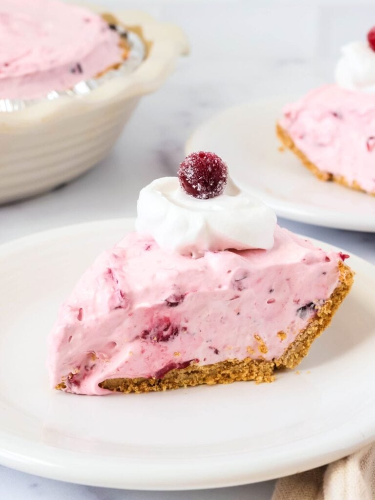 No-Bake Cranberry Pie slice served on a white plate, garnished with whipped cream and a whole cranberry.