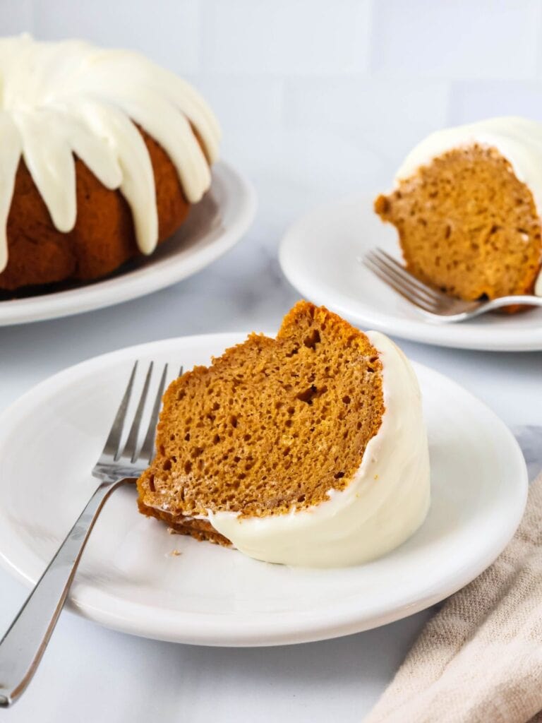 Two slices of pumpkin bundt cake from a mix, served on white plates, with the remainder of the whole bundt cake in the background.