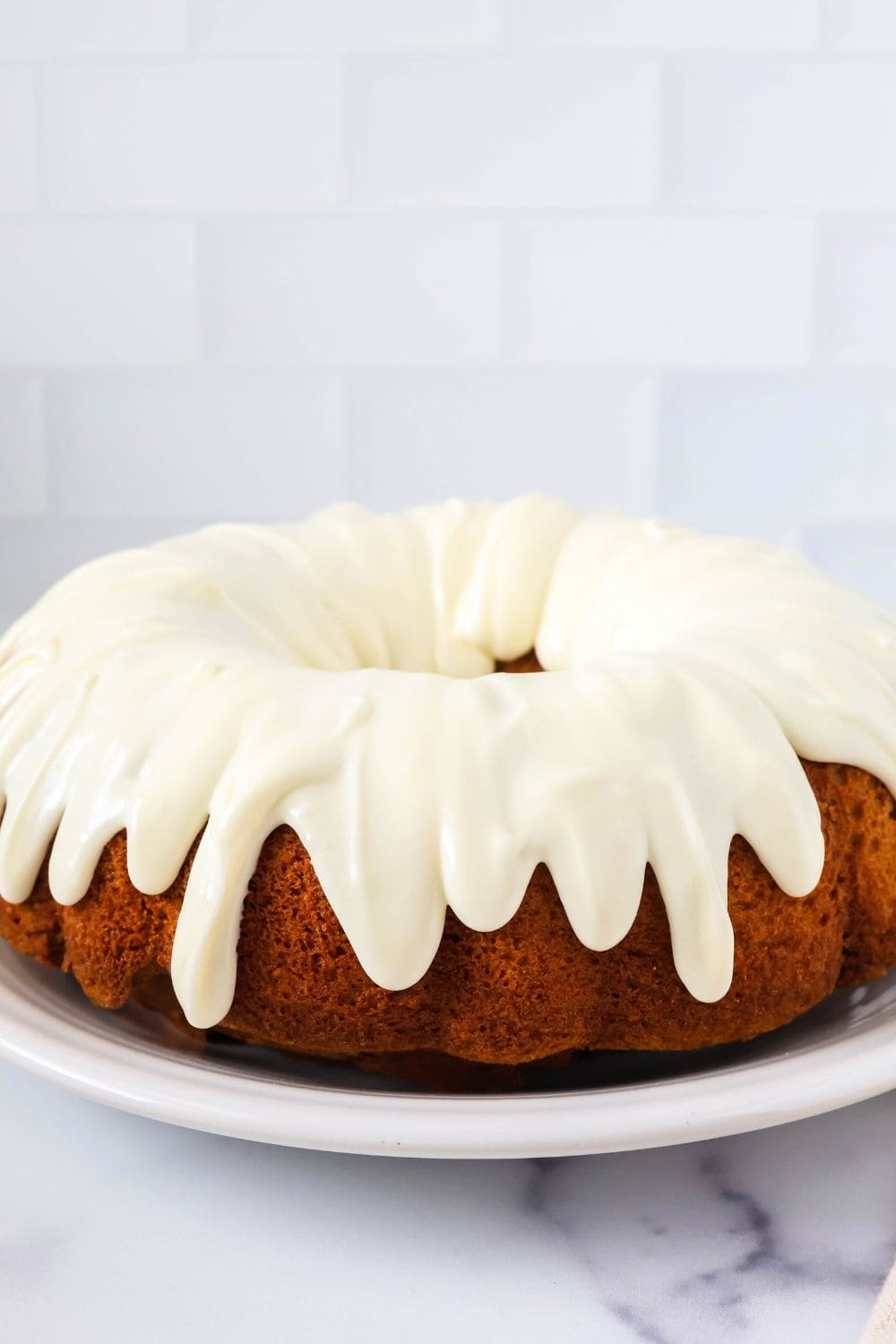 side view of a pumpkin bundt cake made with spice cake mix, drizzled with cream cheese frosting, served on a white plate.