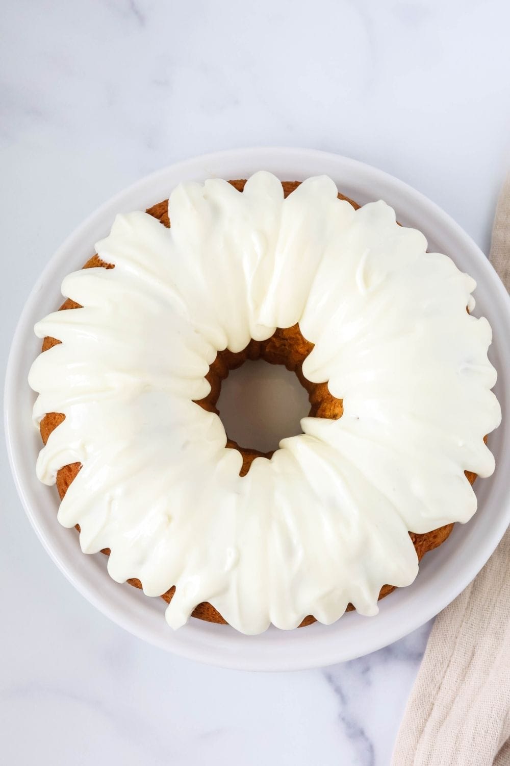 overhead view of a whole pumpkin cake made with cake mix and topped with cream cheese frosting, served on a white plate.