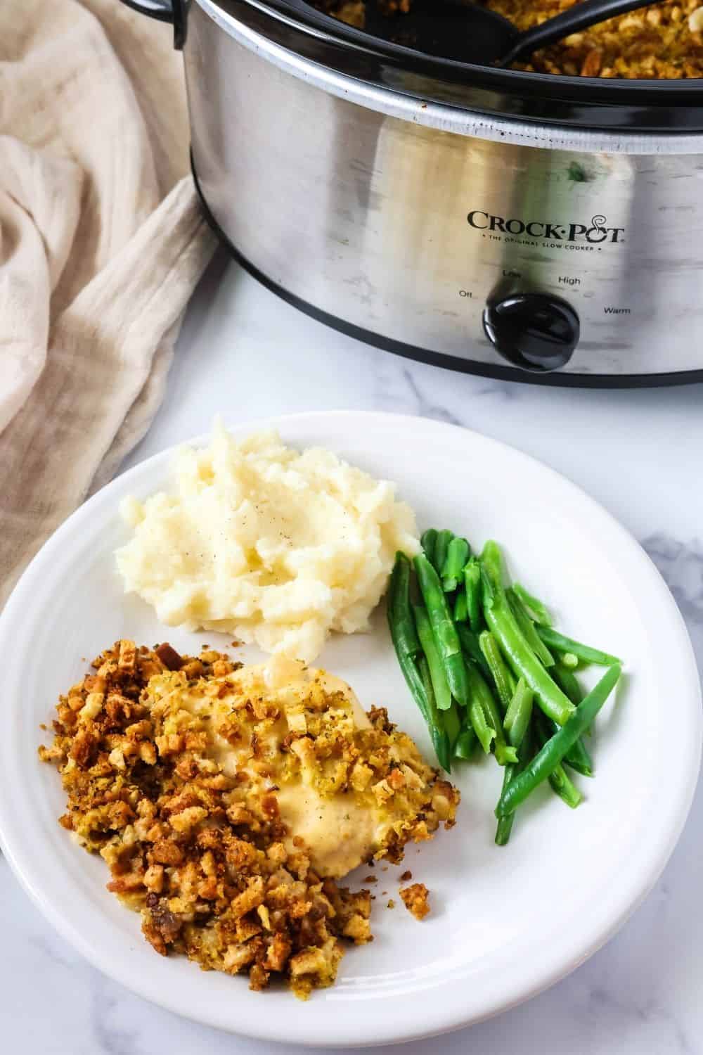 Easy CrockPot chicken and dressing plated alongside mashed potatoes and green beans, with the slow cooker in the background.